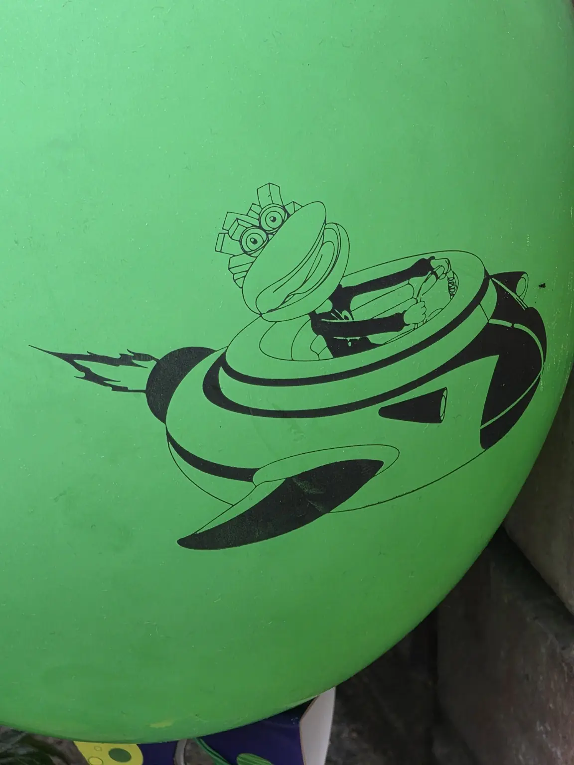Dessin noir sur un panneau vert usé représentant un petit véhicule rétrofuturiste piloté, propulsé par une flamme