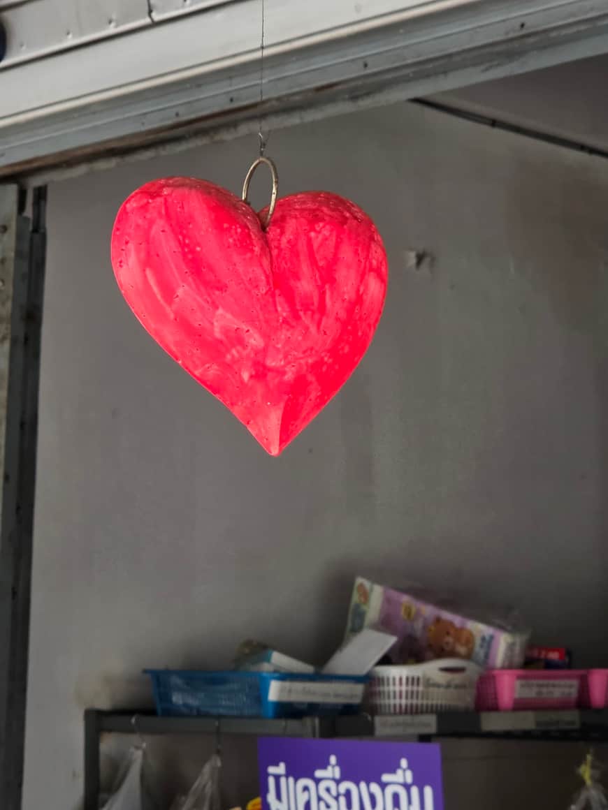 Cœur rouge accroché sur une paroi sombre au-dessus d’une étagère.