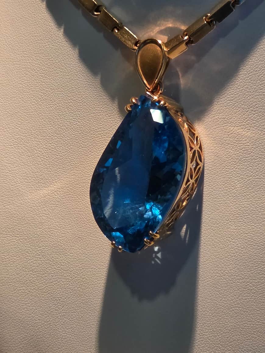 Pendentif bleu serti, présenté dans une vitrine.