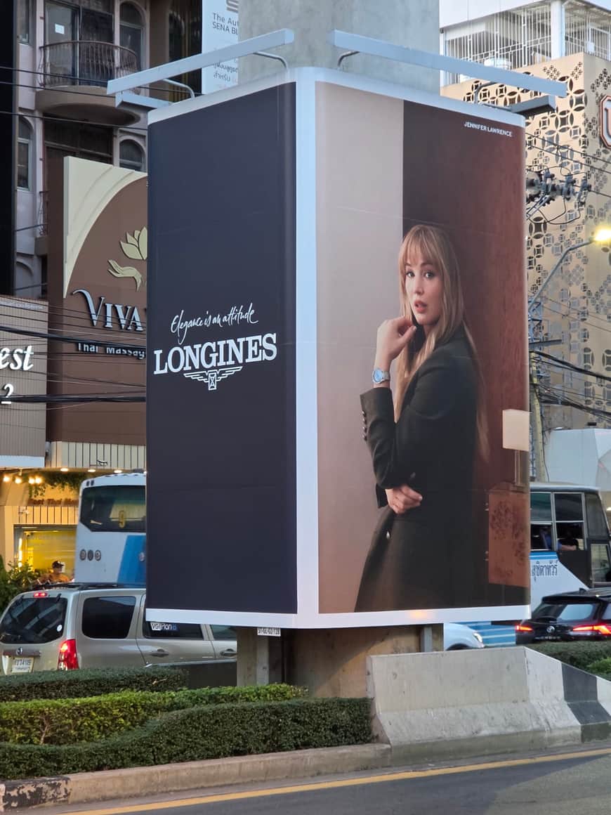 Panneau publicitaire Longines avec une figure féminine, en bord de rue.