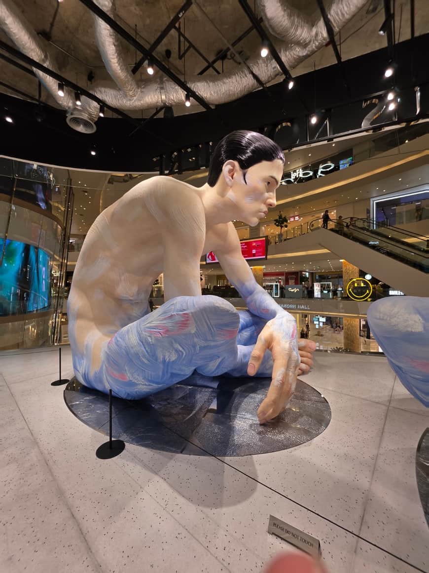 Sculpture figurative assise dans une galerie commerciale.