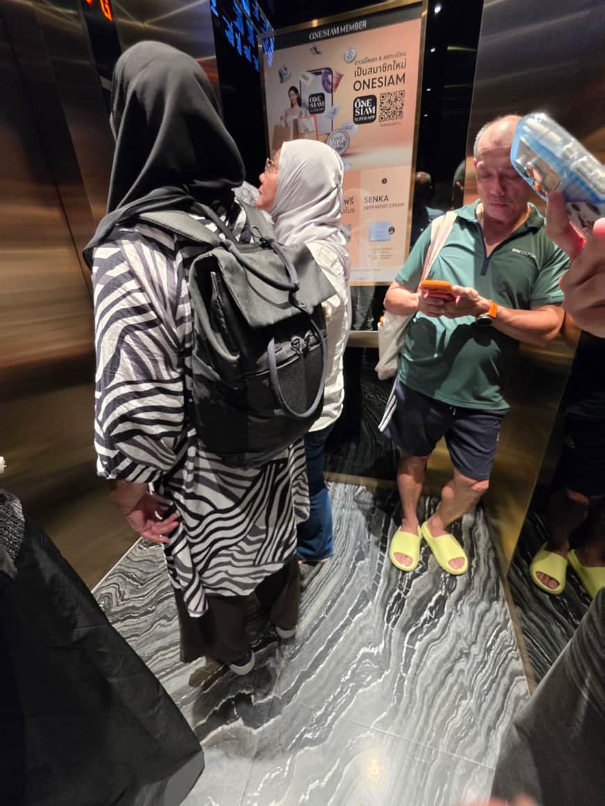 Trois personnes se faisant face dans une galerie, l’une montrant un objet ou un écran.