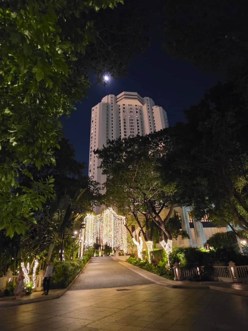Bâtiment éclairé au bout d’une allée nocturne bordée d’arbres.