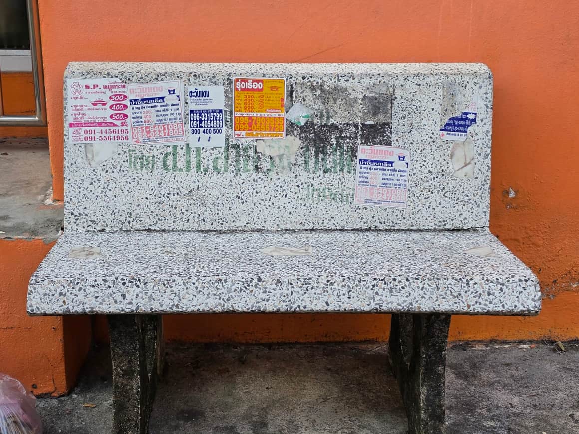 Banc de pierre moucheté contre un mur orangé, avec des inscriptions peintes.