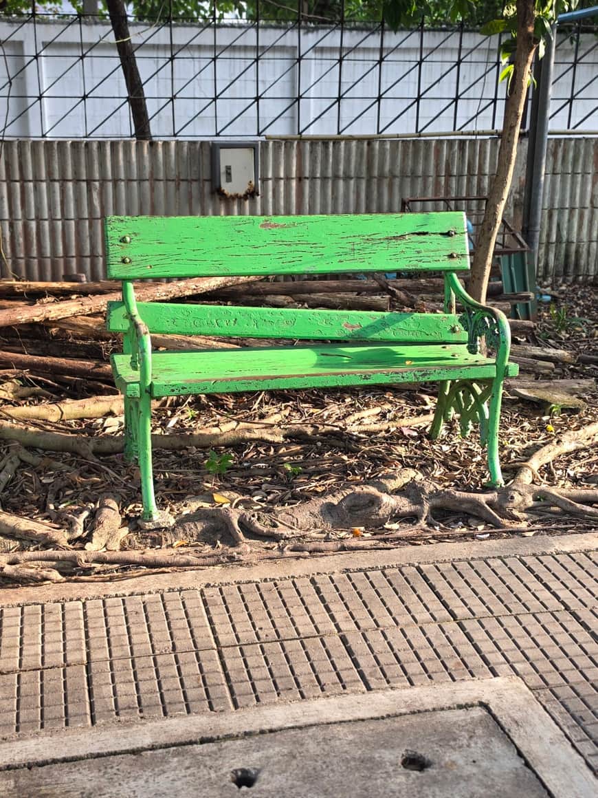 Banc vert dans un petit espace planté derrière une grille.