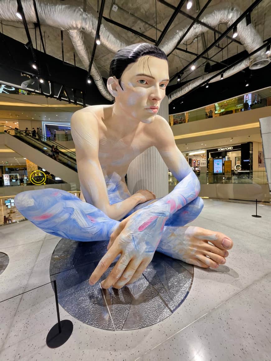 Sculpture figurative accroupie, photographiée de près dans une galerie.