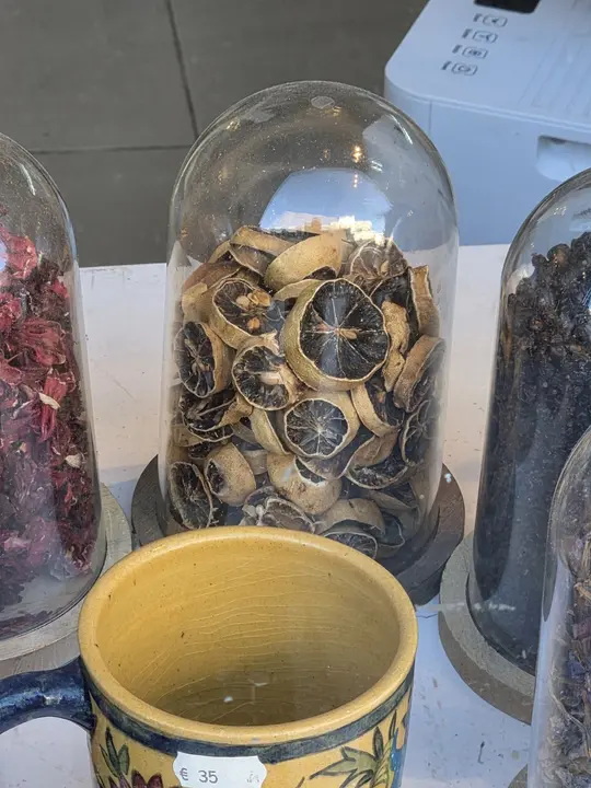 Rondelles d’agrumes séchées présentées sous une cloche de verre, auprès de végétaux secs et d’une tasse jaune