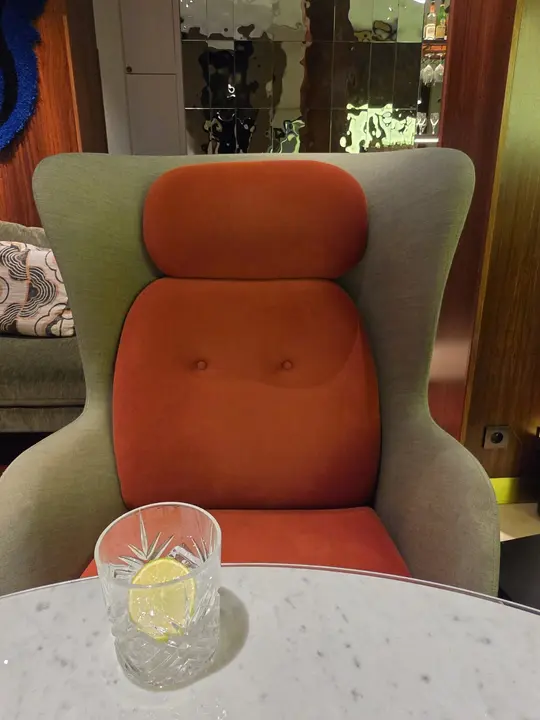 Grand fauteuil vert et rouille auprès d’une table de marbre portant un verre et une rondelle d’agrume