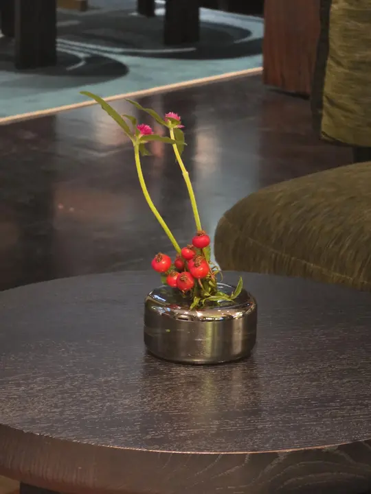 Deux hautes fleurs magenta et des branches chargées de baies rouges dans un vase sombre