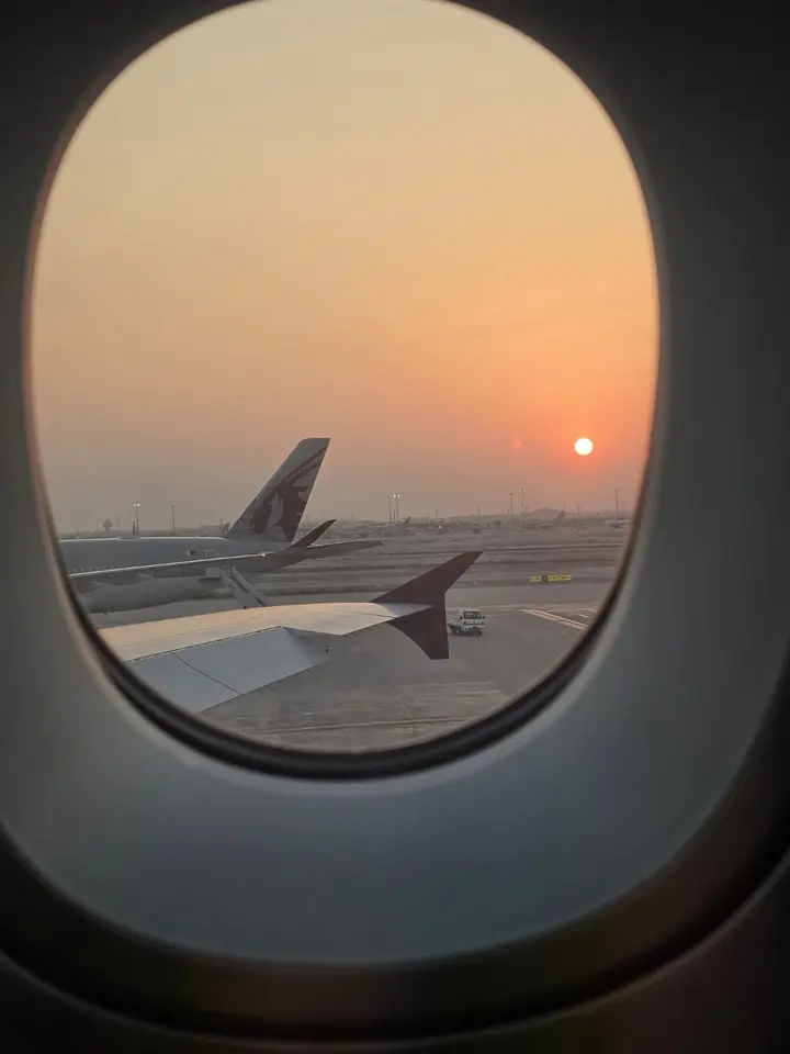 Soleil bas vu par un hublot, au-dessus du tarmac et de plusieurs appareils Qatar Airways.