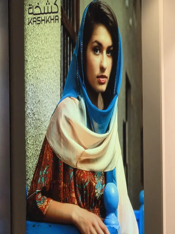 Affiche Kashkha montrant une femme drapée de bleu, blanc et ocre.
