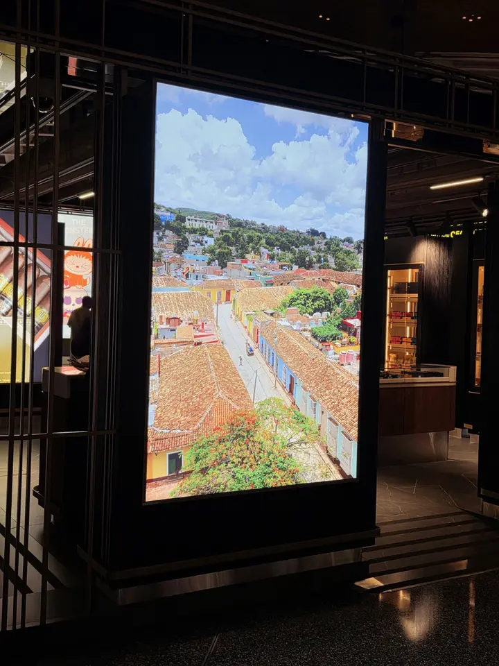 Écran lumineux montrant une ville colorée sous un ciel nuageux, dans un espace commercial sombre.