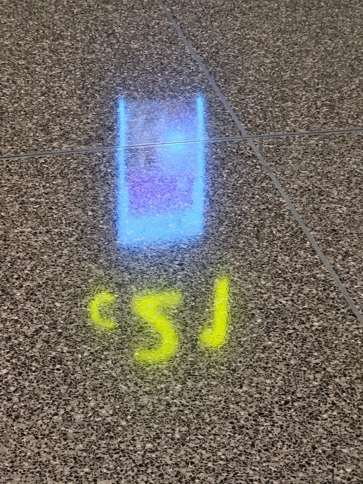 Reflets bleu et jaune d’enseignes lumineuses sur un sol de terrazzo quadrillé.