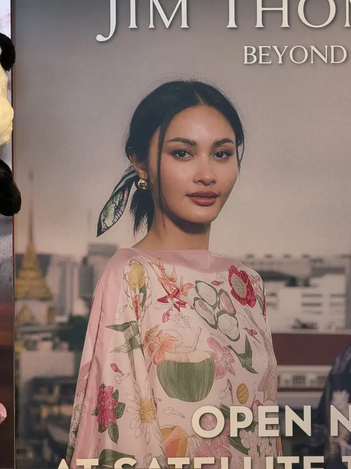 Affiche publicitaire montrant une femme vêtue d’une robe fleurie devant un paysage urbain.