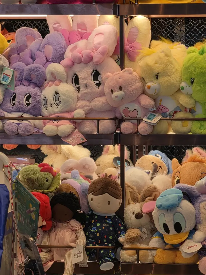 Rayonnage dense de peluches roses, jaunes et brunes derrière une grille sombre.