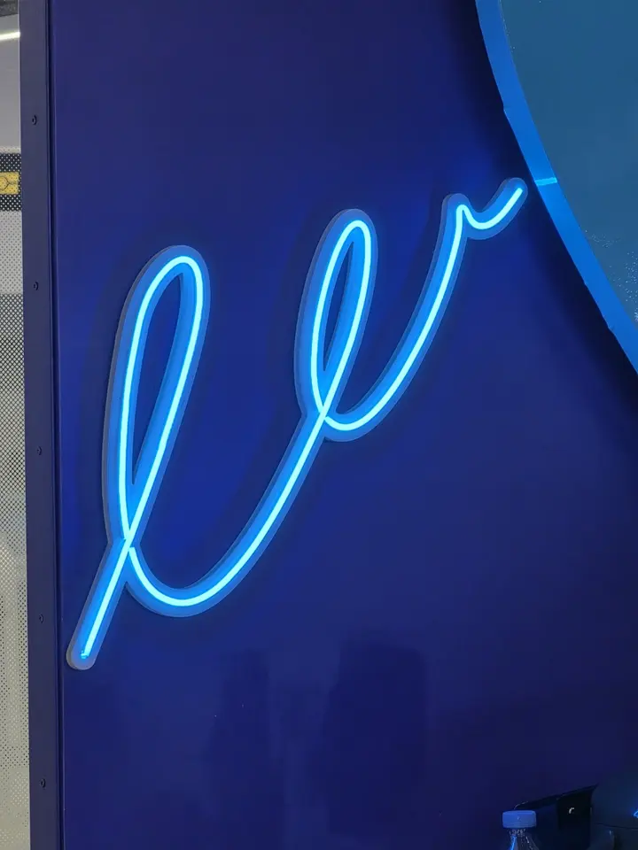 Fragment d’une enseigne en néon bleu formant une courbe lumineuse sur un mur sombre.