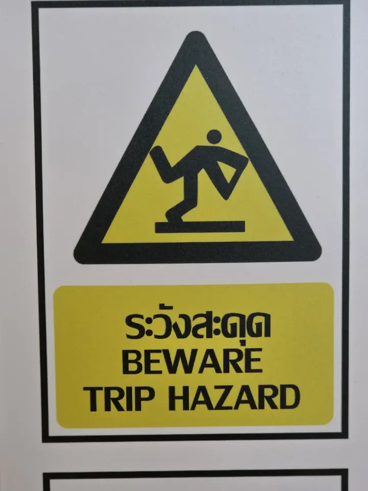 Pictogramme jaune et noir avertissant en thaï et en anglais d’un risque de trébuchement.