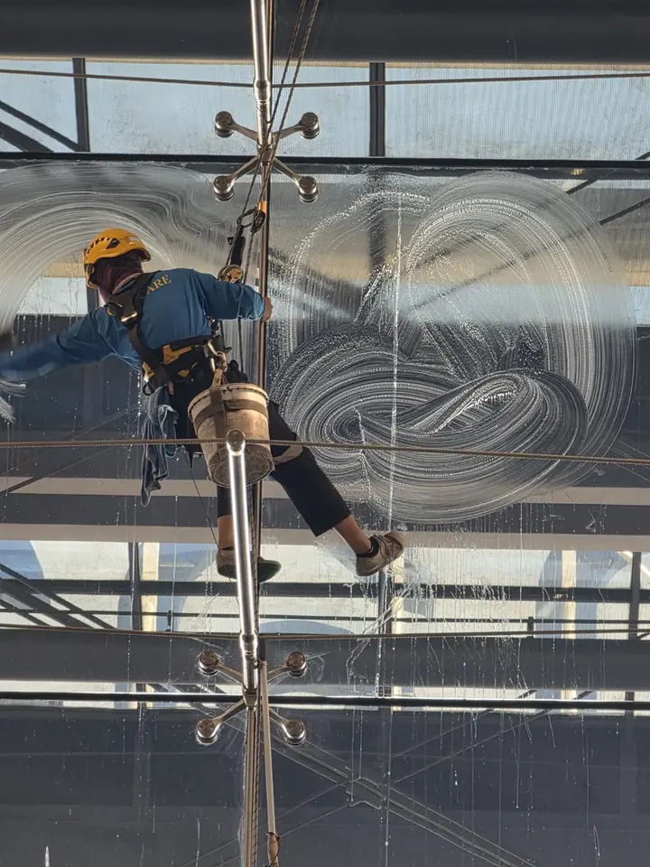 Laveur de vitres suspendu traçant de grands cercles dans la mousse sur une façade vitrée.