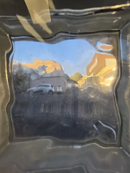Paysage urbain ensoleillé pris dans le reflet irrégulier d’une surface noire.