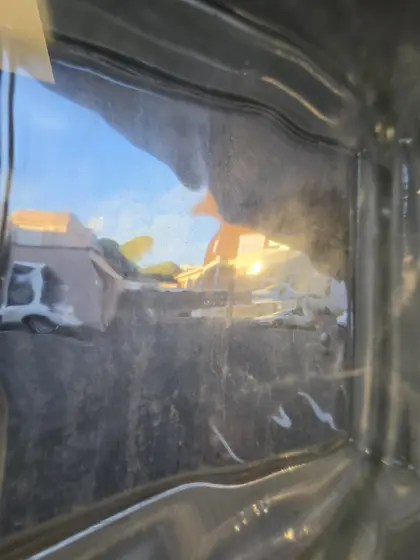 Cour urbaine et soleil reflétés dans une surface noire fortement ondulée.