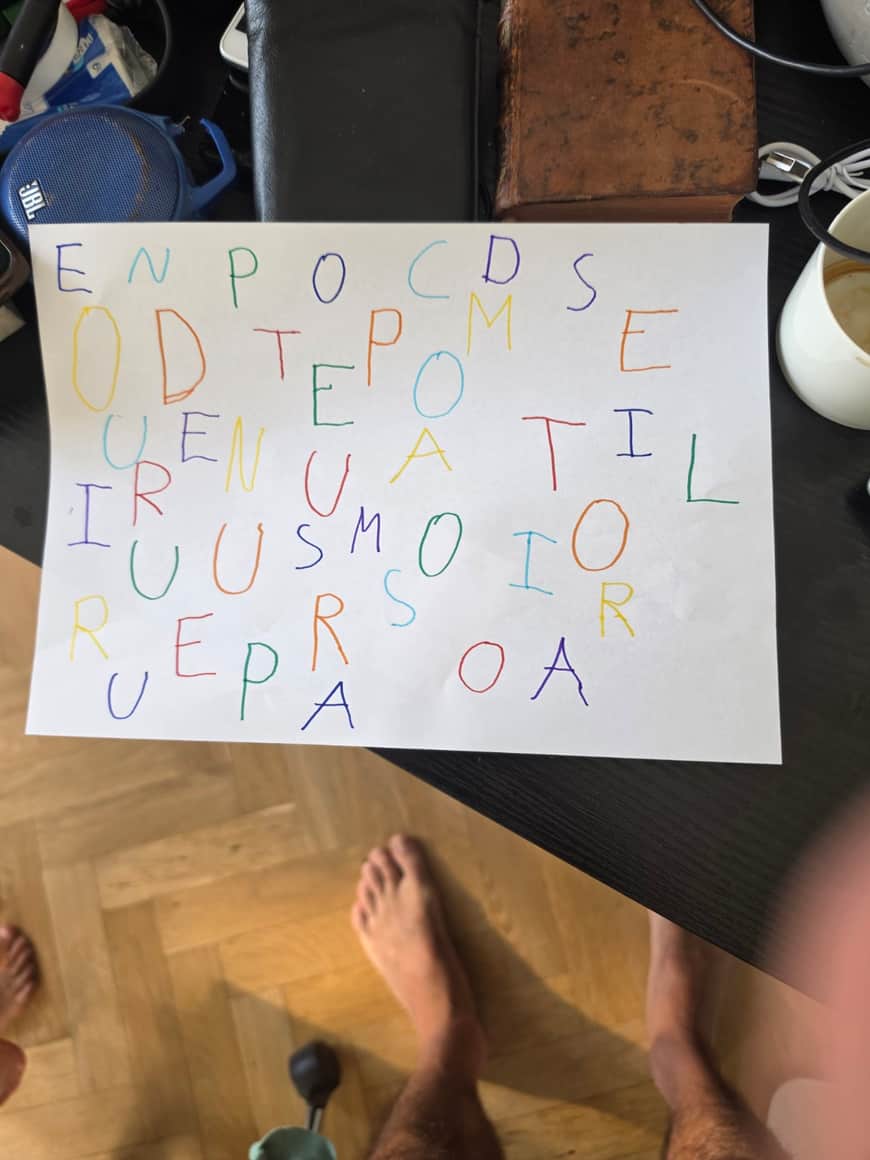 Feuille blanche couverte de lettres capitales colorées et dispersées, posée sur une table domestique.